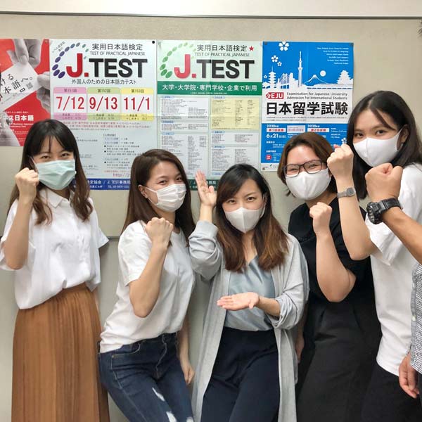 International students posing in front of bulletin board with Japanese tests information